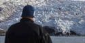 A guest standing on a boat in the foreground looking out at a glacier in the background