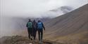 Tre gjester på fottur på en bakketopp med fjell og tåke i bakgrunnen