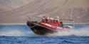 A group of guests and a guide on board a RIB boat sailing on a fjord with mountains in the background