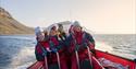 A group of guests on board a RIB boat sailing at speed in a fjord with mountains in the background