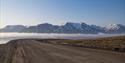 A gravel road in the foreground with a misty valley, a mountainous landscape and a clear blue sky in the background