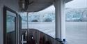 A walkway on board a boat in the foreground with a fjord and a glacier front in the background