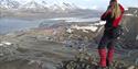 A person standing on top of Platåfjellet looking down on the buildings in Longyearbyen in the background