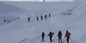 To grupper med gjester på fottur i snødekte omgivelser på vei opp en fjellside