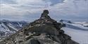 A mountain ridge with the rock formation known as Trolllsteinen, with lightly snow-covered mountains and a cloudy sky in the background