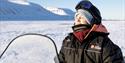 A guest in snowmobile equipment sitting on a snowmobile in snowy surroundings with closed eyes enjoying the sunshine