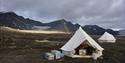 Two white tents in a tent camp in the foreground, with a tundra and mountain landscape in the background