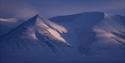 A snow-covered mountainous landscape in blue twilight conditions