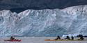 A group of guests and a guide paddling in kayaks with a glacier in the background