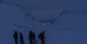 Several people and a dog on their way to the ice cave, with Longyearbyen, mountains and a fjord in the background