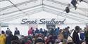 A crowd sitting in a festival tent eating, with a "Taste Svalbard" logo and a line of tables with food for sale in the background