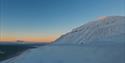 Solstråler fra midnattssola som treffer en fjelltopp