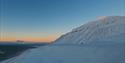 Solstråler fra midnattssola som treffer en fjelltopp