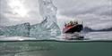 Halv-undersjøisk bilde av isfjell med RIB-båt ved siden av i gråvær.