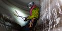 Ice cave climbing. Lady attached with safetyropes and carabiner to the frozen cavewall