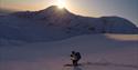 A person skiing down a mountain with powdersnow. Sunset, clear sky and a mountain in the background.