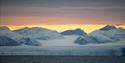 Snødekte fjell og isbre i kveldssol.