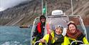 Tre personer smiler på RIB-båt med fjell i bakgrunnen.