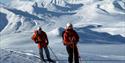 Two people on their way up a mountain on skis with blue sky and endless with snowcovered mountains in the background