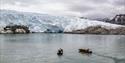 To RIB-båter foran stor isbre i stille fjord.