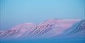 A mountain formation is bathed in blue and pink light.