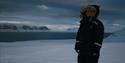 Person wearing snowmobileclothing, standing in the dark snowcovered winterlandscape.