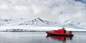 RIB-båt på fjorden foran snødekt landskap.
