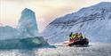 RIB-båt nær stort isfjell i arktisk landskap.