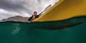 Picture taken partly over, and partly under water, of a person paddling a kayak.