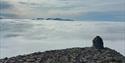 Summit towering over a low cloud cover, with mountains in the background.