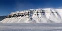 The snow-covered Tempelfjellet stands majestically on its own with a blue sky in the background.