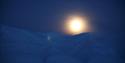 Bright full moon above the dark blue snowcovered mountains