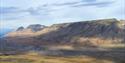 Green gras and a smal river in a valley with big mountains in the background