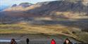 People walking up a hill with a river and mountains in the background