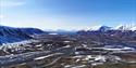 Landscape that is a bit covered in snow. Surrounded by snowcovered mountains with the ocean in the horizon