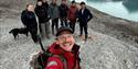 A guide is taking a selfie with a group of people with a glacier in the background