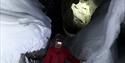 A person walking inside an ice cave. The entrence to the ice cave is visible in the background