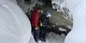 Two people standing inside a ice cave with head lamps on