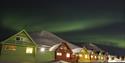 Fargerike hus i Longyearbyen med snødekte fjell og nordlys på himmelen i bakgrunnen