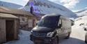 A minibus parked in front of a building with snow-covered mountains in the background