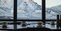 A table with coffee cups in the foreground with a snow-covered mountainous landscape behind the window in the background