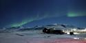 En hundegård i en snødekt dal med nordlys på himmelen i bakgrunnen