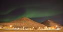 Northern lights in the skies over two mountains and buildings in Longyearbyen