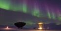 Two radar antennas pointed towards a clear starry sky with northern lights in purple and green colours in the background