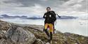 A guide with a backpack hiking up a hill with a fjord and mountains in the background