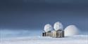 Tre antenner på KSAT sin bakkestasjon for satelitter omringet av snø med en mørk himmel i bakgrunnen