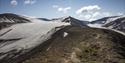 A group of people hiking along a mountain ridge with mountains, glaciers and a blue sky in the background