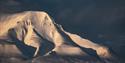 A mountain illuminated by the sun in the middle of an otherwise dark landscape