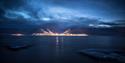 We stand on the opposite side of the river, looking at Longyearbyen from a distance. The lights in the town meets a sky with deep blue hues and dark c