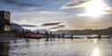 A group of guests and guides pulling kayaks on shore with sunshine and a partially clouded sky in the background